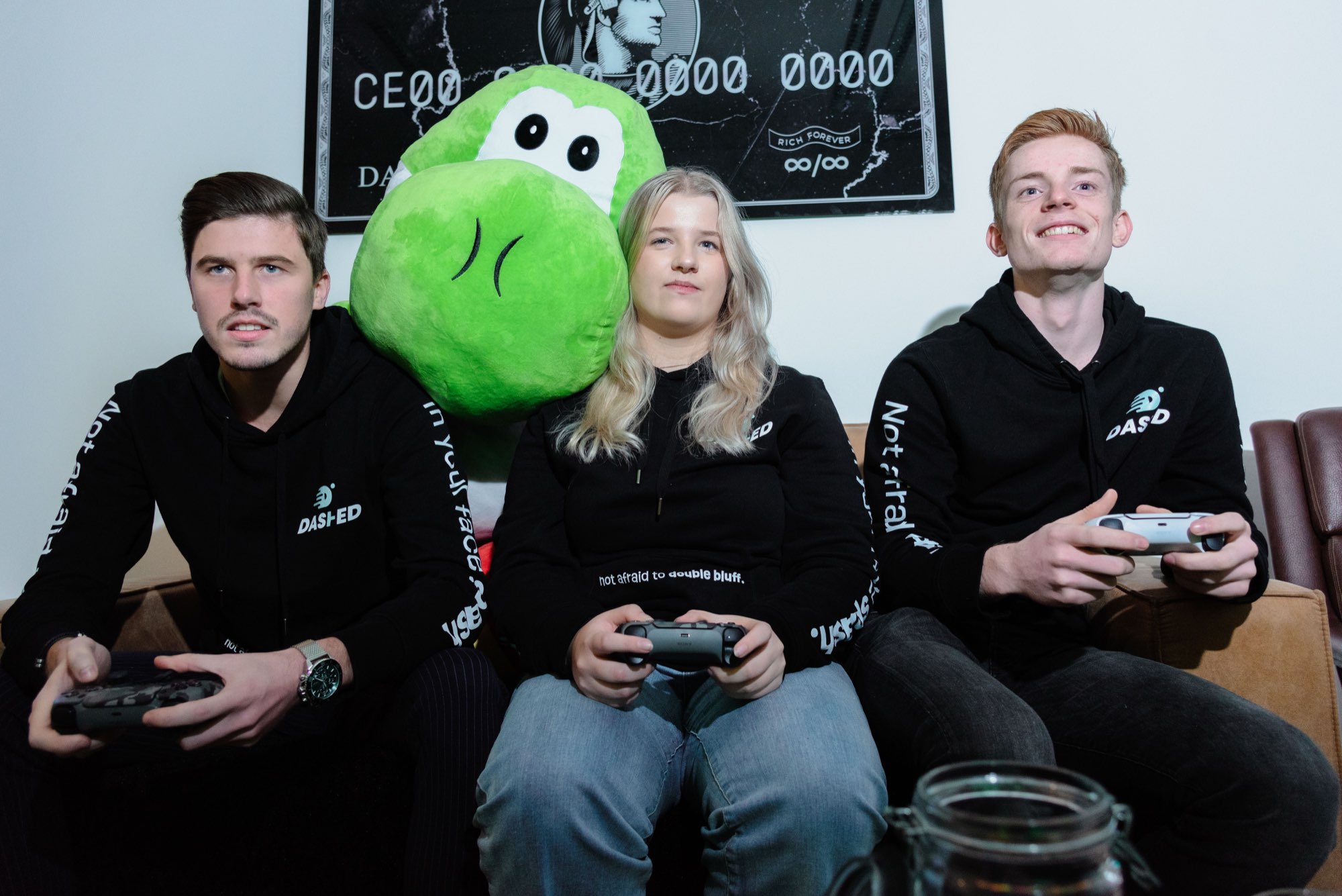 Drie collega's met controllers en de groene mascotte op de bank