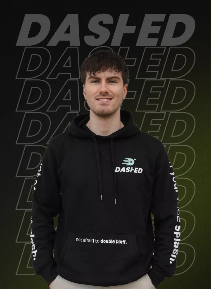Een persoon draagt een zwarte hoodie met het logo "DASHED" en de tekst "not afraid to double bluff". De achtergrond herhaalt het woord "DASHED" meerdere keren.
