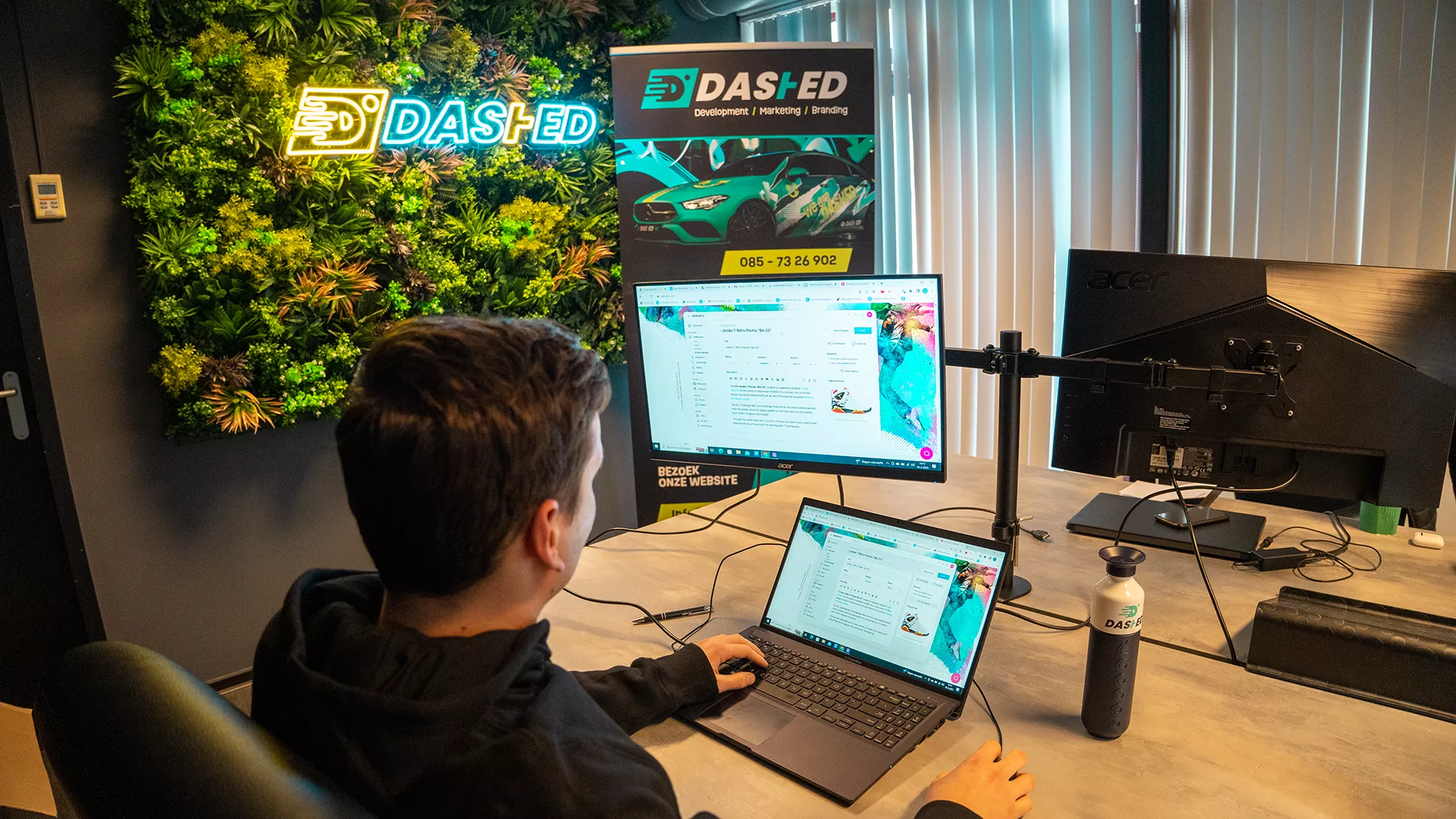 Man werkt op laptop en monitor in kantoor met groene wand en DAS+ED-logo.