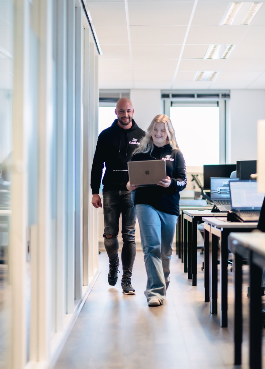 Twee collega's lopen samen door de kantoorgang met een laptop