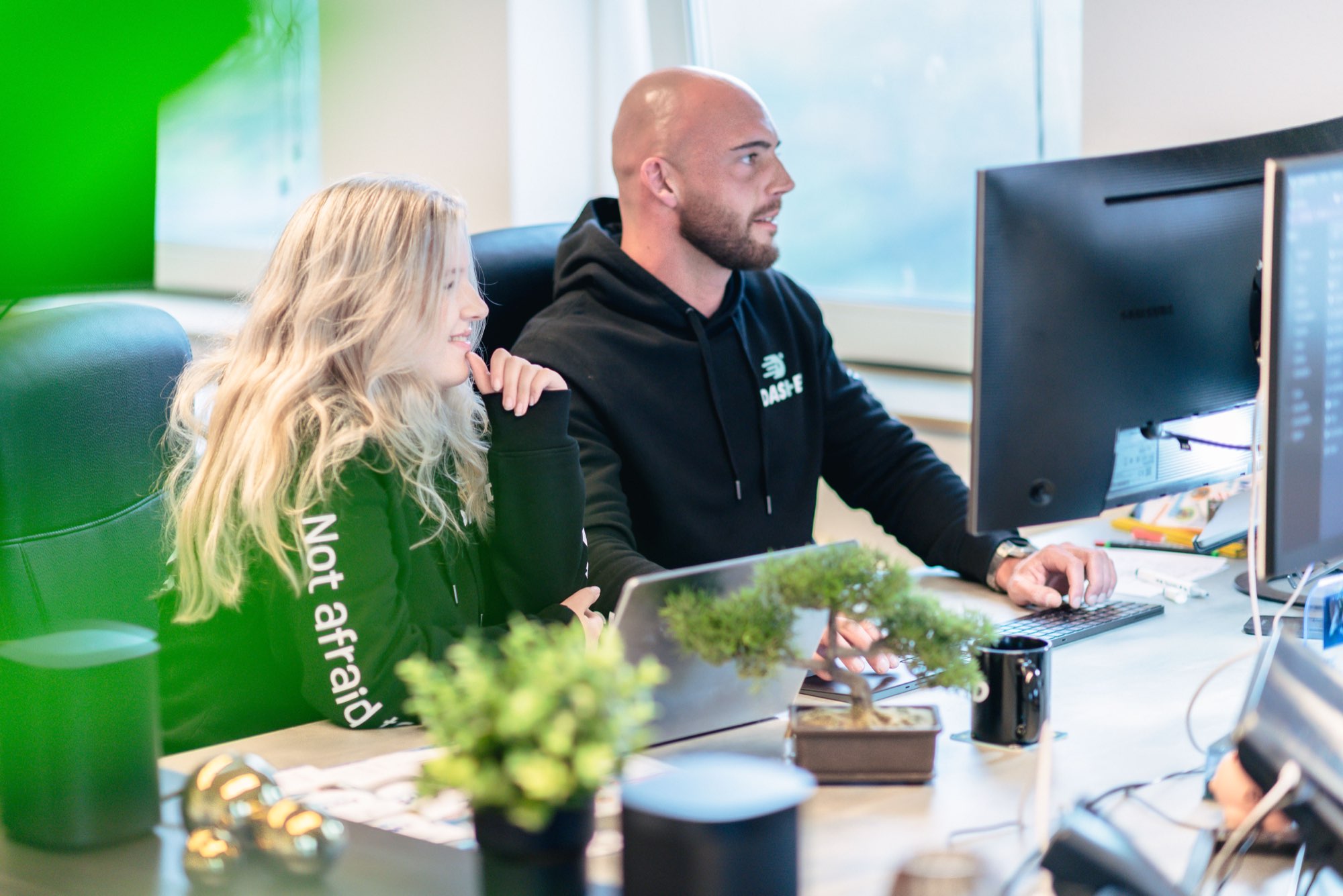 Twee collega's overleggen achter een scherm voor een groene wand