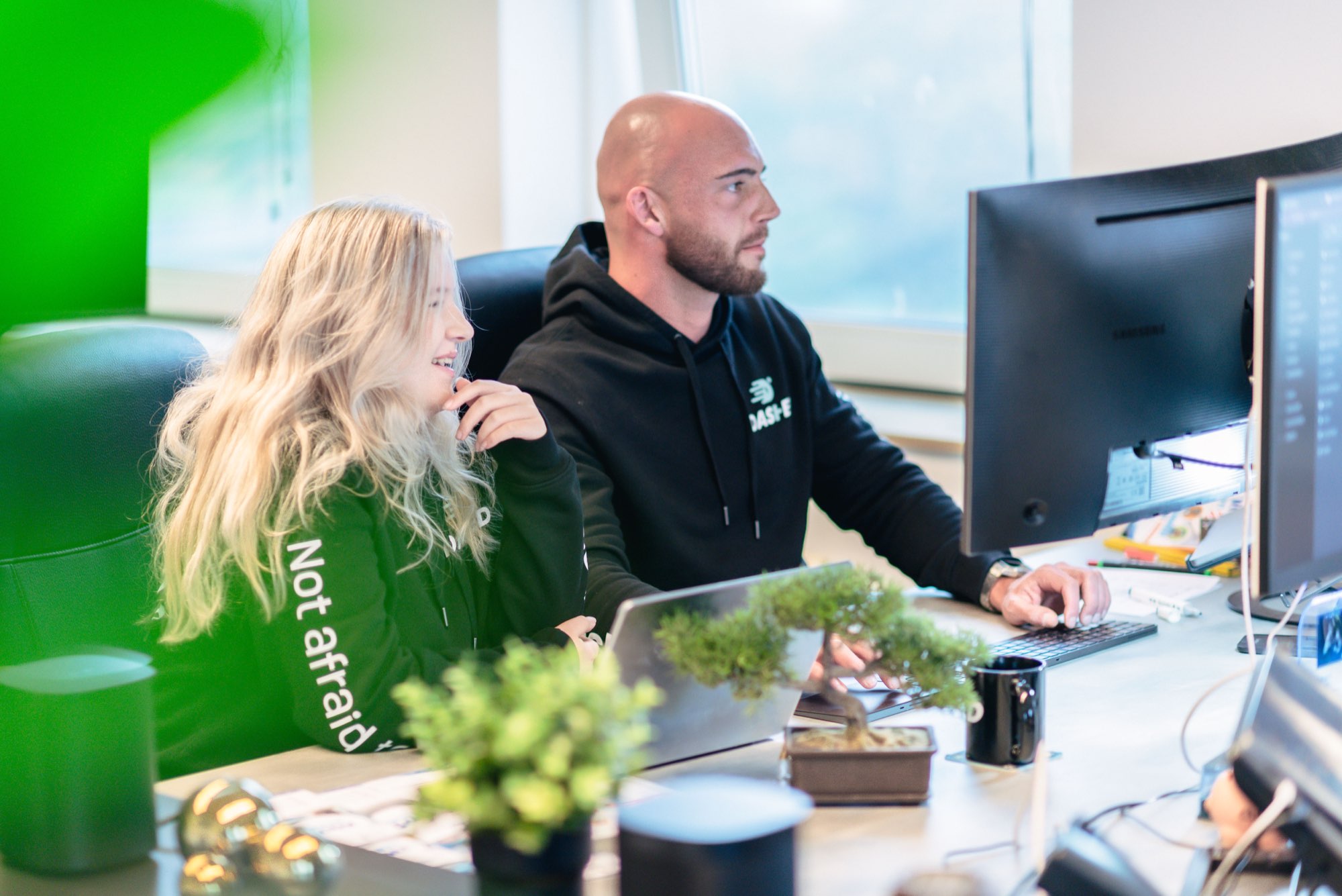 Twee collega's overleggen achter hun werkplek met planten