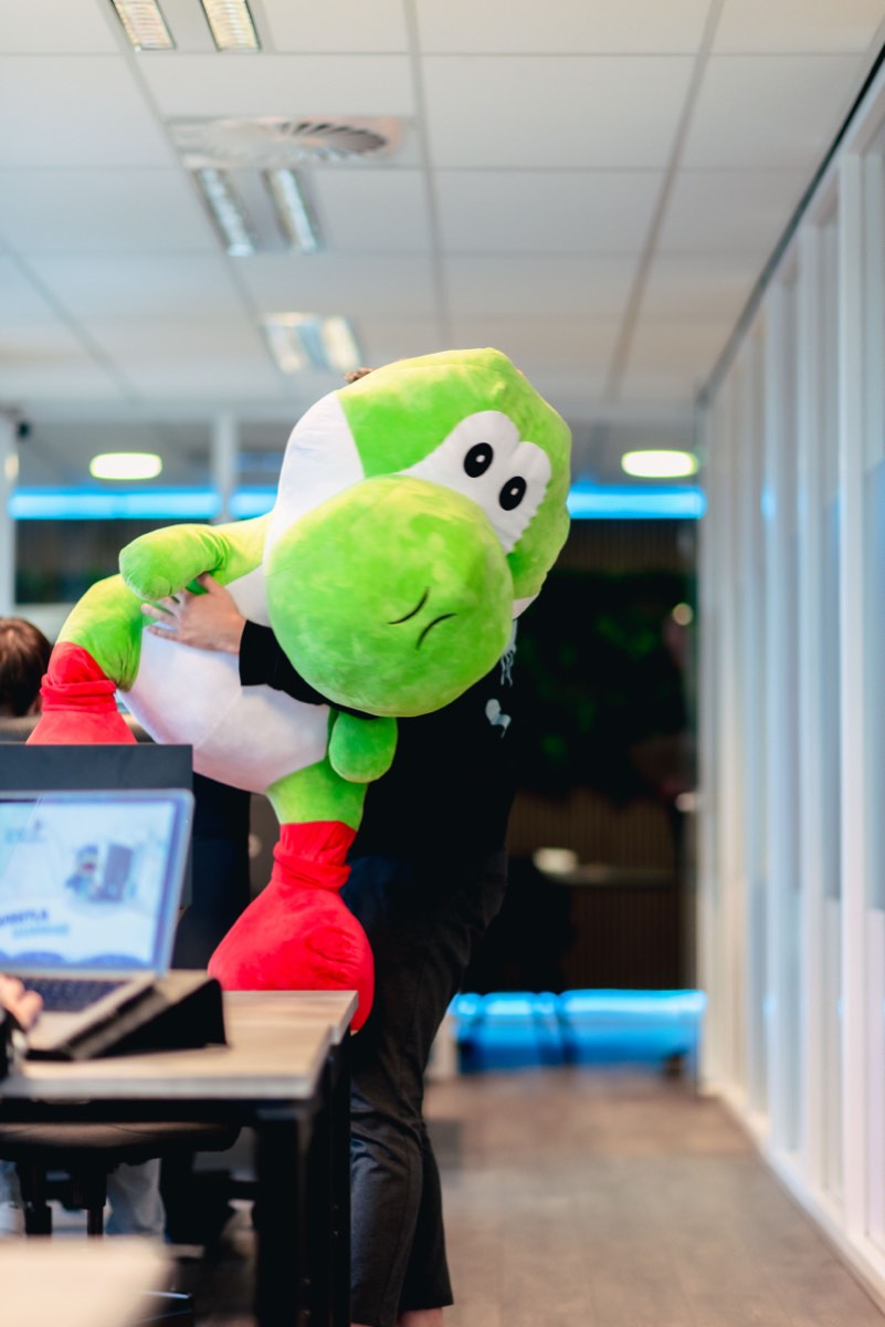 De groene Dashed-mascotte staat bij een werkplek