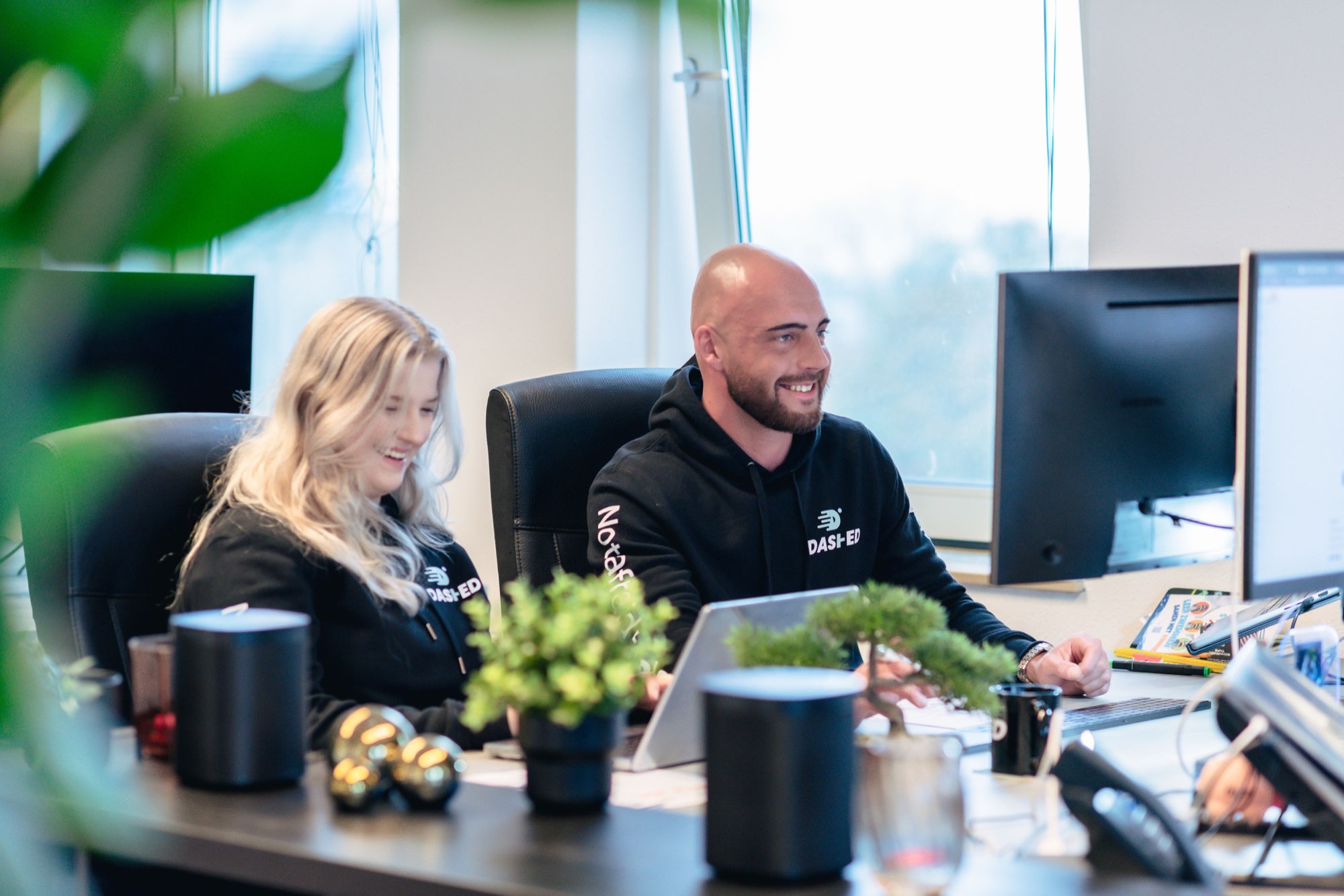 Twee collega's lachen samen achter hun werkplek met planten