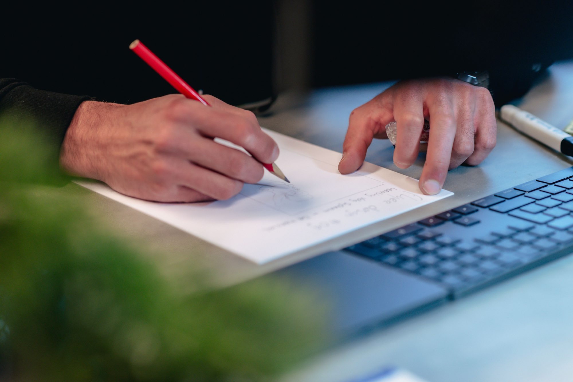 Iemand maakt aantekeningen met een rode pen naast een laptop