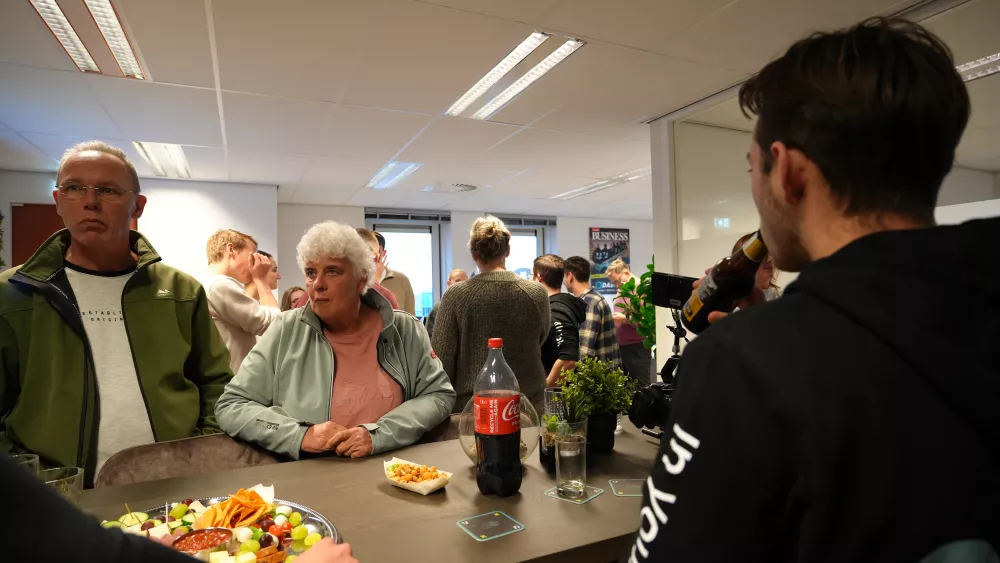 Mensen in een kantoorruimte tijdens een informele bijeenkomst. Op de voorgrond staan schalen met snacks en frisdrank, terwijl een groep mensen in gesprek is op de achtergrond.
