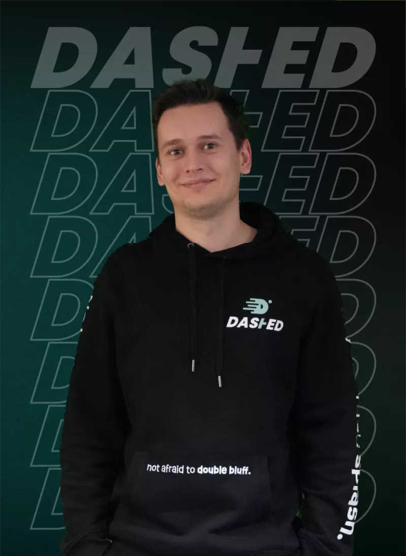 Persoon in een zwarte hoodie met het merk "DASHED" op de borst, tegen een achtergrond met herhaalde tekst "DASHED".