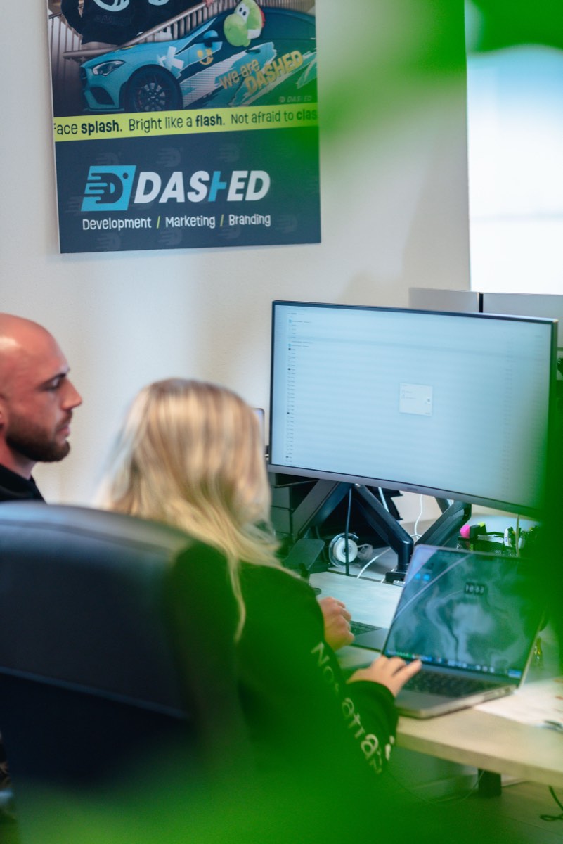 Twee collega's overleggen achter een scherm bij een Dashed-banner
