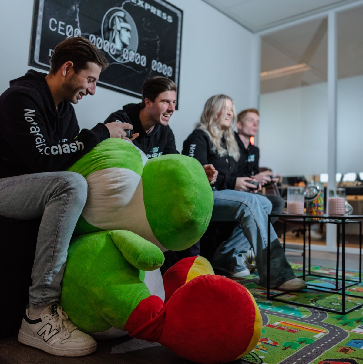 Collega's op de bank met de groene mascotte en gamecontrollers