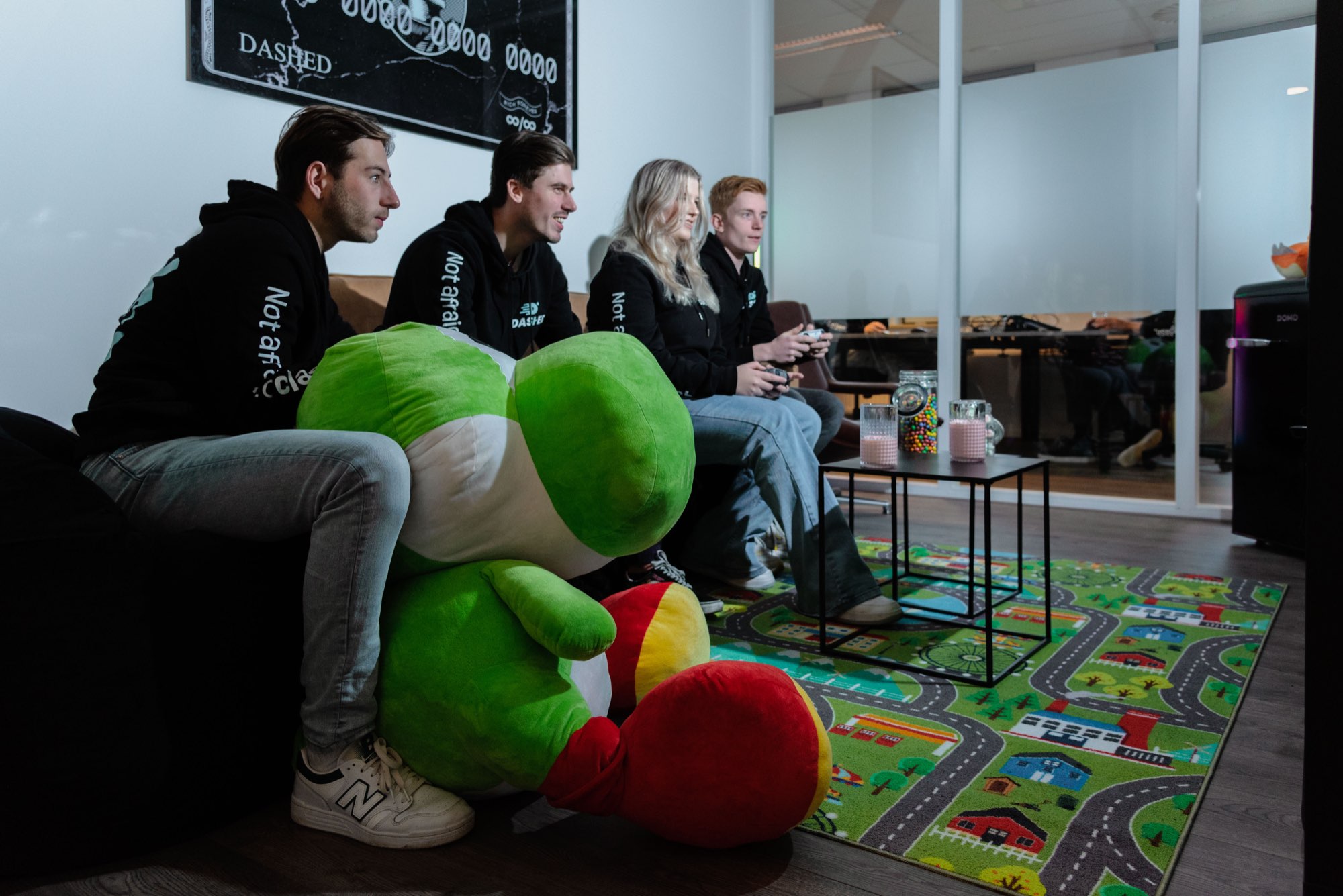 Collega's op de bank met gamecontrollers en de groene Dashed-mascotte