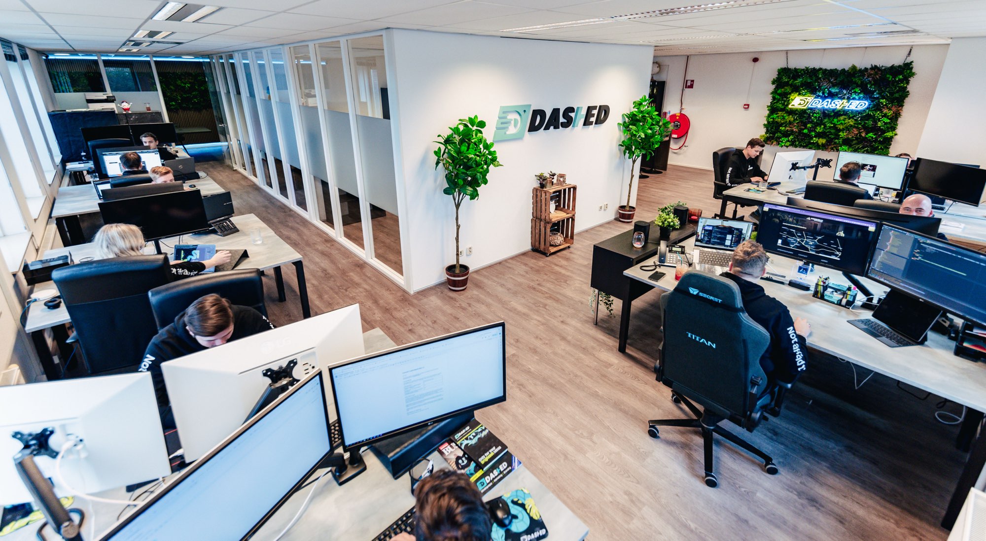 Kantoortuin met bureaus, monitoren en de Dashed-logowand