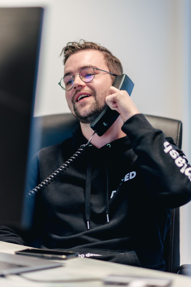 Medewerker met bril lacht tijdens een telefoongesprek