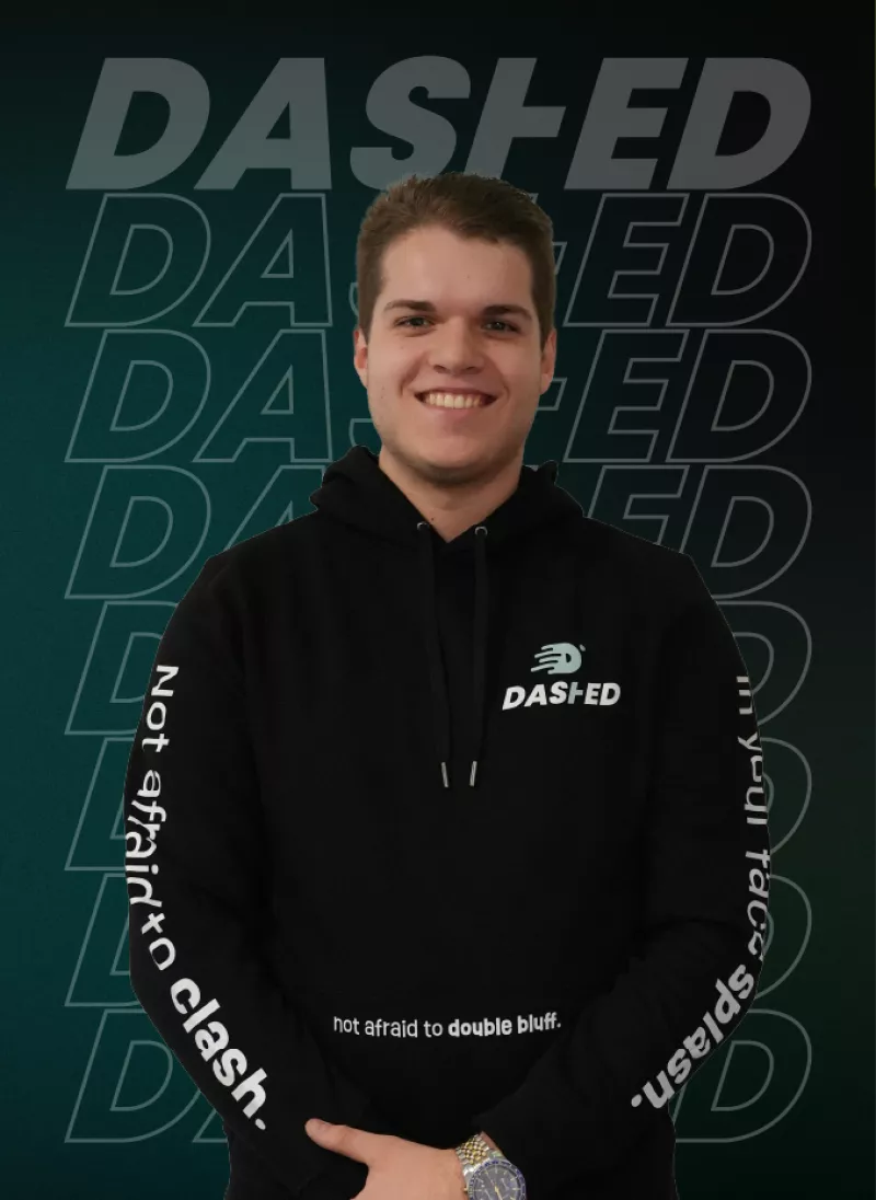 Man in zwarte hoodie met het logo "DASHED" en teksten op de mouwen. Achtergrond heeft herhalende tekst "DASHED". Hij lacht breed, handen gevouwen voor zich.
