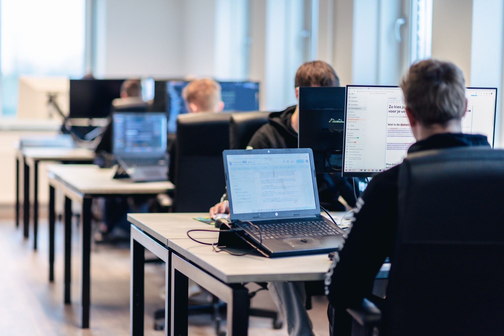 Twee collega's werken achter hun bureau met laptop en monitor