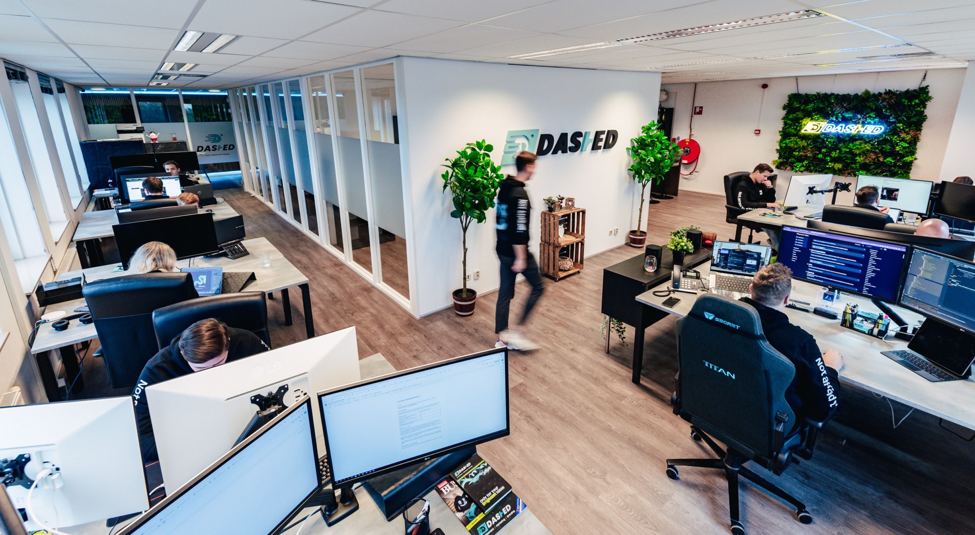 Kantoortuin met werkplekken en een medewerker bij de logowand