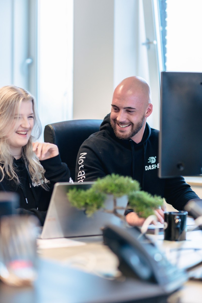Twee collega's overleggen lachend achter hun schermen